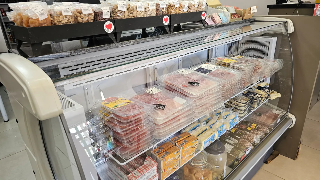 Balcão refrigerado com queijos e frios embalados, e castanhas a granel na bancada acima
