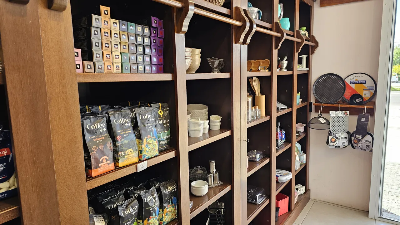 Estante de madeira com cafés em pacote, cápsulas, louça e utensílios de cozinha